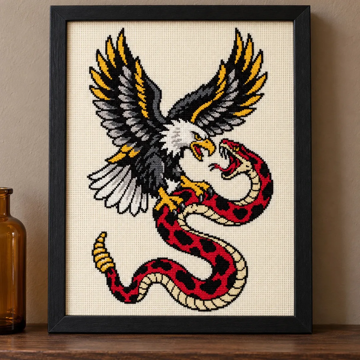 Straight-on view of the finished Eagle and Snake Cross Stitch in a black frame on a wooden shelf