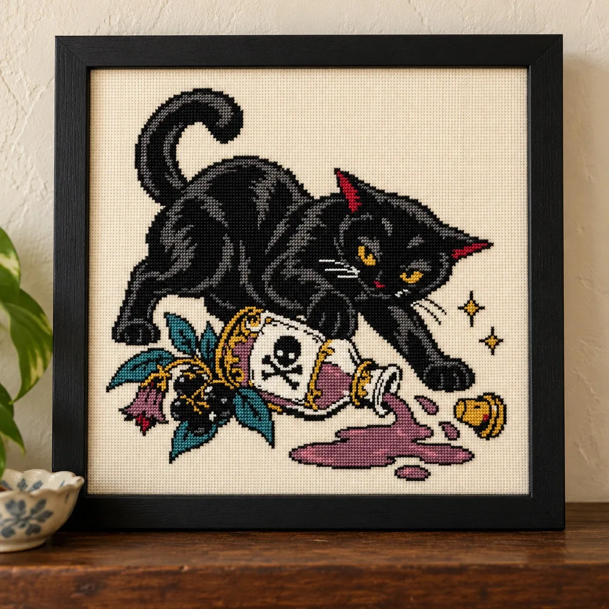 Black cat knocking over a poison bottle, cross stitch in a black frame on a wood shelf